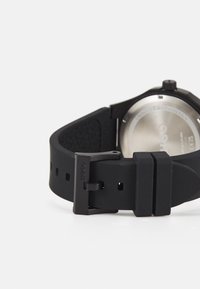 Black silicone watch strap with a textured surface, featuring a silver stainless steel case back and a black metal buckle.