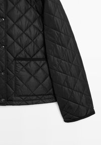 Zwarte gewatteerde jas met diamantpatroon, voorzien van drukknopen en een voorzak met een getextureerde rand. Zachte, gladde stof.