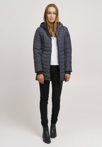 Gray padded jacket with a hood, front zipper, and textured pattern. Paired with black fitted pants and ankle boots.