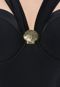 Costume da bagno nero con scollatura a V profonda e spalline incrociate, con un accento centrale a conchiglia dorata metallica. Tessuto dal tocco liscio.