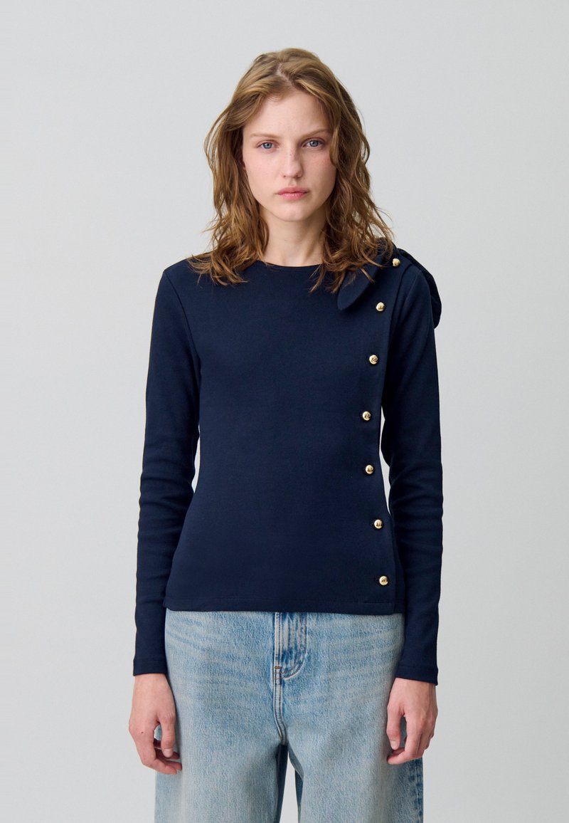 Maglia a maniche lunghe color navy con bottoni dorati sul lato sinistro, con un'accenno a fiocco sulla spalla, realizzata in un tessuto elastico e strutturato.