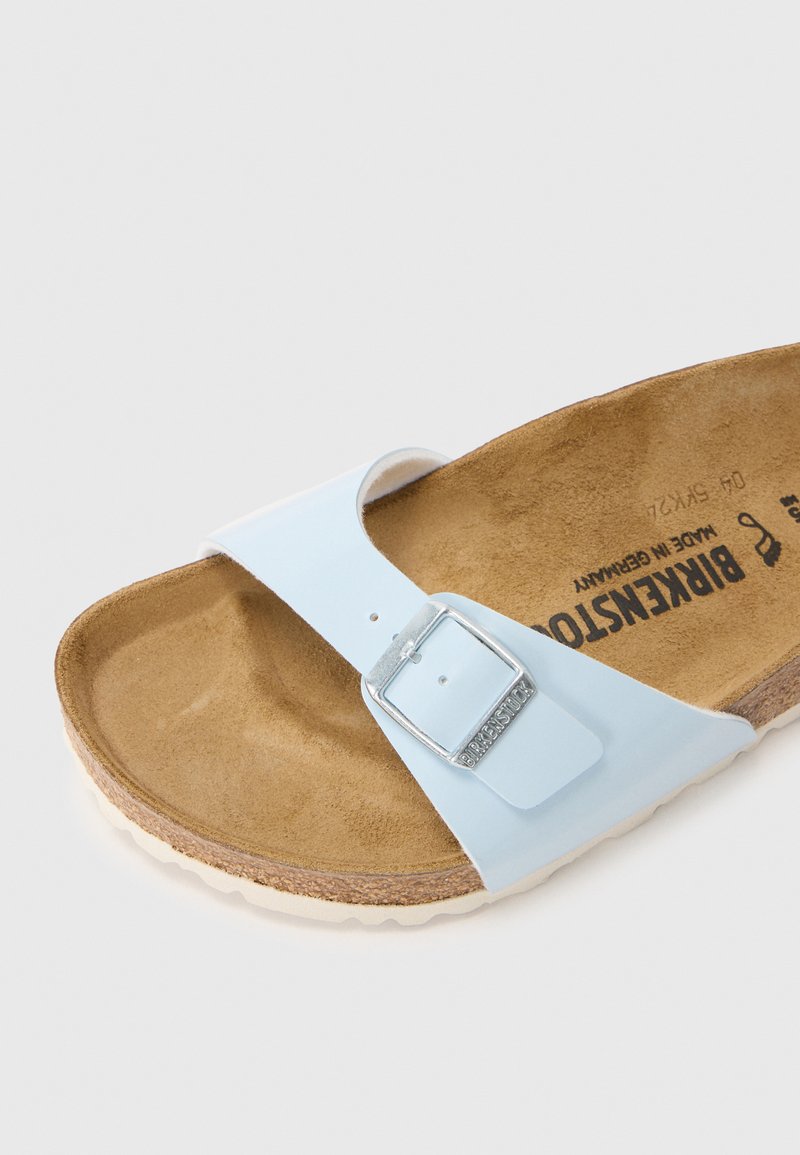 Lichtblauw plastic sandaal met een gestructureerde bruine kurken voetbed en een zilveren gespaccent, met een witte zool en een plat ontwerp.