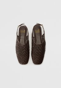 Zapatos slingback trenzados en marrón con un diseño de punta abierta y un tacón sólido. Cuentan con un forro interior suave y un pequeño acento dorado en la correa.