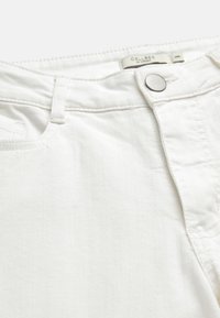 Hvide denimjeans i nærbillede, der viser knap, linning, bæltestrop og syninger omkring frontlommen med synligt mærkeindvendigt i livet.