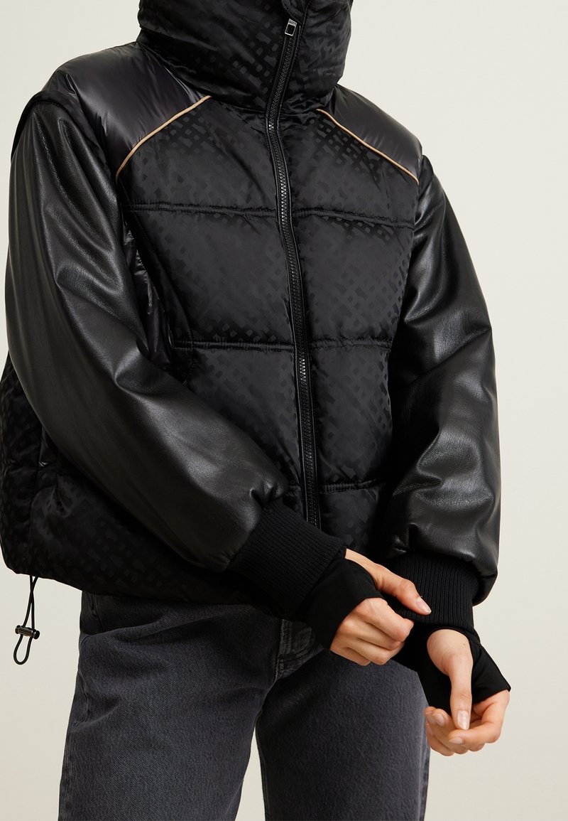 Schwarze Federjacke mit glatten Lederärmeln, hochstehenden Kragen, Reißverschluss, gerippten Bündchen und strukturierten Mustern am Körper.