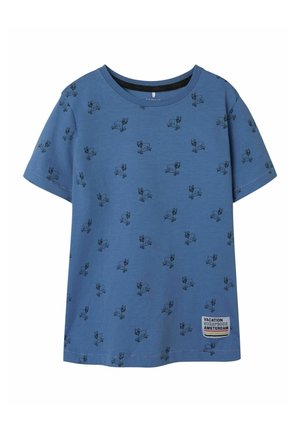 Blå kortärmad t-shirt i mjuk bomull, med ett upprepat tryck av en svart tecknad hund och en vit etikett med texten "Semesteralbum Amsterdam."