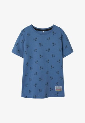 Plava majica kratkih rukava od mekog pamuka, s ponovljenim crnim uzorkom crtanog psa i bijelom etiketom s natpisom "Putni album Amsterdam."