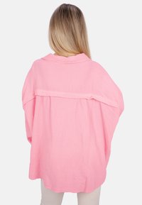 Übergröße, leichtes Hemd aus weichem, pinkfarbenem Stoff mit strukturierter Oberfläche, ausgestattet mit einem Kragen und einem Rückenfalten-Detail für zusätzliche Form.