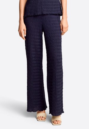 Pantalon large texturé bleu marine porté avec des sandales beiges à bout ouvert et talon carré, visible de la taille aux pieds.
