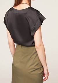 Schwarze Satinbluse mit kurzen Rollärmeln, kombiniert mit einem taillierten olivgrünen Rock. Glatte Textur und minimale Nähte sind sichtbar.