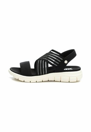 Sándalo negro con múltiples correas elásticas y una plantilla acolchada. Presenta una suela blanca texturizada y un pequeño detalle de logo en el costado.
