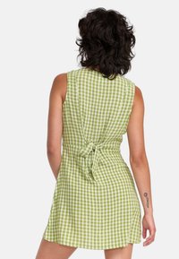 Robe en vichy vert avec un corsage ajusté et une jupe évasée. Dispose d'un détail noué dans le dos et d'une conception sans manches. Fabriquée en tissu léger.