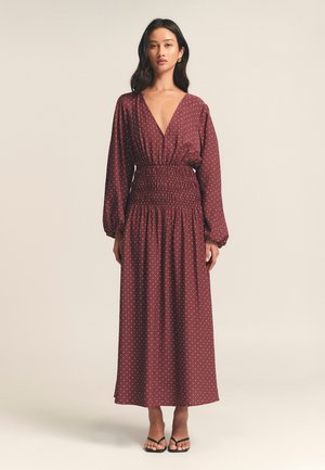 Burgunderfarbenes langes Kleid mit weißen Punkten, V-Ausschnitt, gerafftem Taillenbereich und langen Puffärmeln. Glattes Material mit fließender Silhouette.