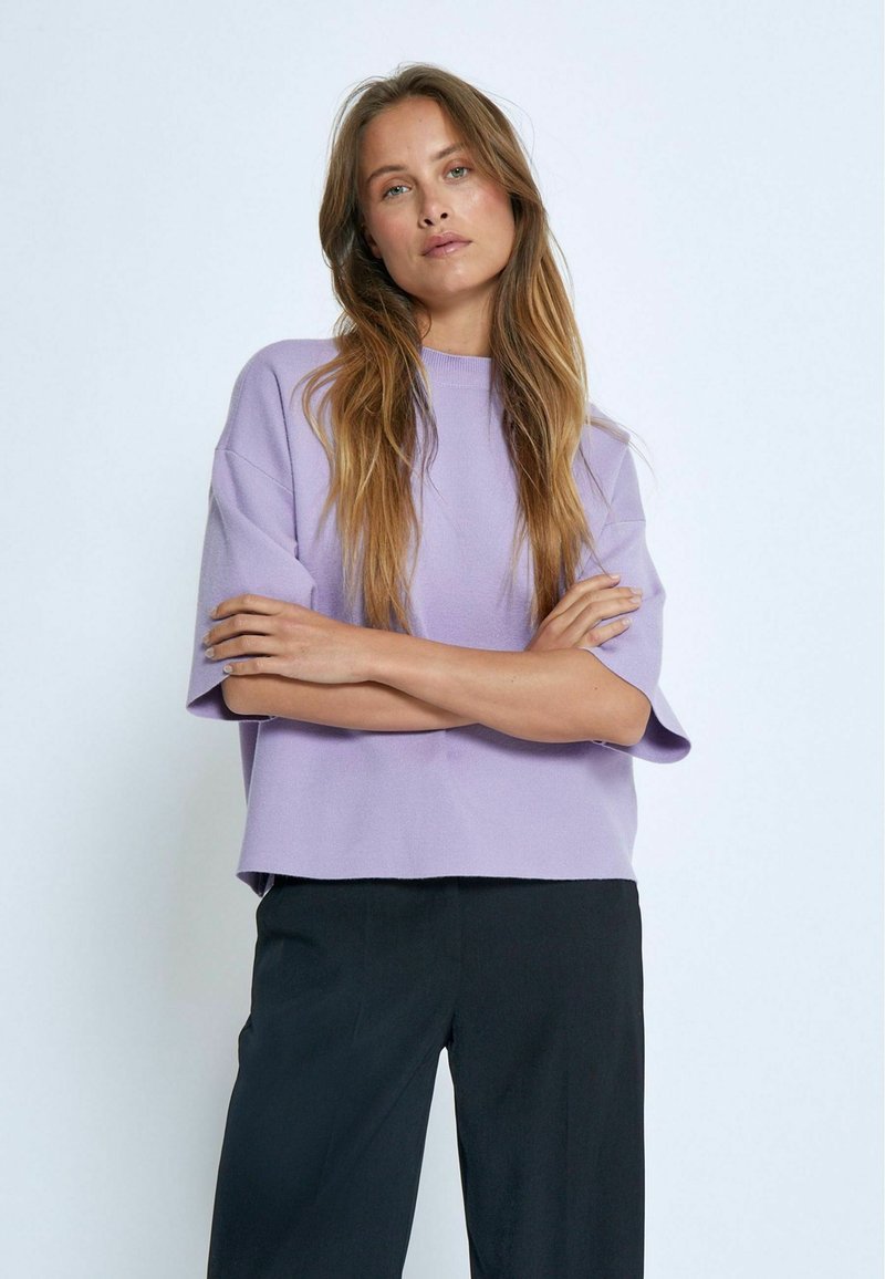 Pullover corto lavanda a maniche corte con scollo rotondo, vestibilità ampia, tessuto morbido e orlo dritto, abbinato a pantaloni neri.