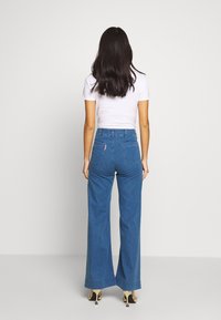 Breda denimjeans i en mellanblå tvätt. Har fem fickor och en sydd logotagg bak. Tillverkad av bomull med en slät struktur.