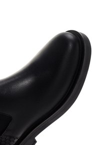 Botín de cuero negro hasta el tobillo con un acabado suave, puntera redondeada y un panel lateral texturizado. Cuenta con una suela de goma negra duradera.