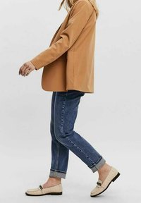 Vaalea ruskea bleiseri, siniset käärityt farkut ja kermahaluiset loaferit, joissa on teksturoitu pinta ja koristeelliset yksityiskohdat.