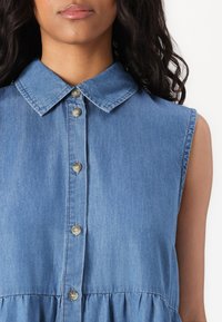 Τζιν φόρεμα με επαναλαμβανόμενο λαιμό, κοντά μανίκια, κουμπιά μπροστά, ανοιχτό μπλε χρώμα και gathered μέση για προστιθέμενη υφή.