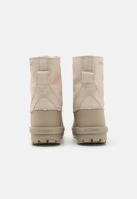 Beige vinterstøvler med myke nubuck-skinn, gummisåler og teksturerte detaljer. Har en liten logo på hælen og en bakløype for enkel påføring.