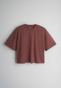 T-shirt manches courtes, coupe carrée, rouge brique atténué avec un col rond, présenté sur un fond uni gris clair.