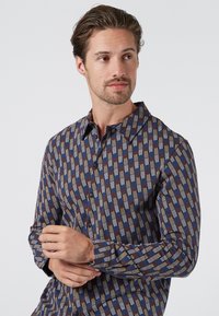 Camisa de botones de manga larga con un patrón geométrico multicolor en tonos azules, marrones y crema. Tela de algodón con un cuello estructurado.