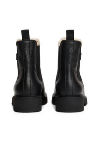 Une paire de bottes en cuir noir avec une surface texturée, une semelle épaisse, des languettes de tirage et une doublure en shearling crème visible, montrées de l'arrière.