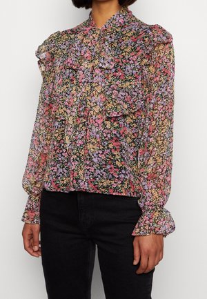 Blumenbluse aus durchsichtigem Stoff in Schwarz, mit kleinen rosa, lila und gelben Blumen, Rüschensaum und ausgestellt geschnittenen Ärmeln.