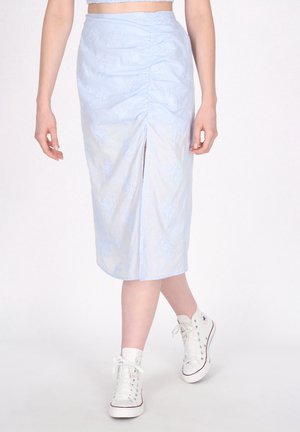 Gonna midi azzurro chiaro con texture arricciata, motivi floreali ricamati e uno spacco frontale. Abbinata a sneakers alte bianche.
