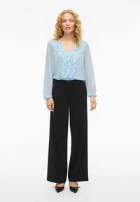 Lyseblå chiffonbluse med volangt krage, kombinert med høytlivs svarte vide bukser og svarte spisse hæler.