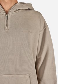 Béžová mikina s kapucňou a polovičným zipsom, predná kapsa a jemné logo. Mäkko štruktúrovaná tkanina s voľným strihom.