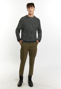 Pulover alb-negru cu model stropit, cu gât rotund, asortat cu pantaloni cargo verzi măslinii care au două buzunare laterale și ghete de luptă negre.