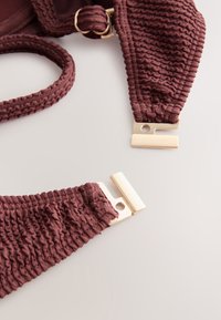 Close-up of ribbed textured brown fabric bikini top with gold metal clasp and adjustable strap on light surface.
