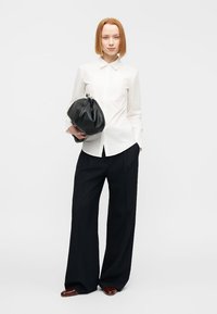 Λευκό πουκάμισο με κουμπιά και μακριά μανίκια, συνδυασμένο με μαύρο παντελόνι σε φαρδιά γραμμή με λεπτές ρίγες. Μαύρη δερμάτινη τσάντα με στρογγυλεμένο σχήμα.