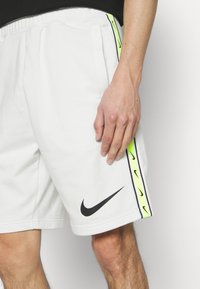 Shorts sportivi bianchi con logo Nike nero, caratterizzati da una striscia verde neon e nera sui lati. Tessuto morbido e liscio, cintura elastica.