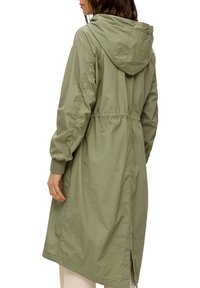 Leichte, olivgrüne Parka mit Kapuze, tailliertem Schnitt und elastischen Bündchen. Verfügt über seitliche Schlitze für mehr Bewegungsfreiheit und eine strukturierte Stoffoberfläche.