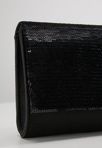 Pochette noire avec détails en sequins sur le devant, dos en tissu lisse, forme rectangulaire, sans aucune quincaillerie visible.
