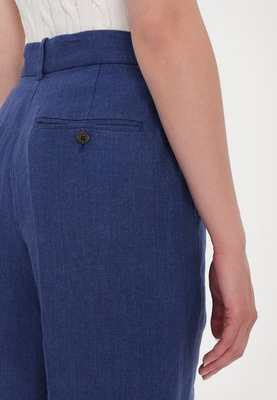 Pantalon en lin bleu avec une coupe ajustée, featuring une poche arrière et une fermeture à bouton. Texture lisse et motif de tissage subtil visible.
