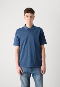 Σκούρο μπλε πόλο μπλουζάκι από βαμβάκι, με κλείσιμο τριών κουμπιών και κεντημένο λογότυπο στο στήθος. Βραχίονες κοντοί, κλασική εφαρμογή.