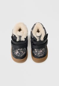 Melnie sporta apavi ar ziedu rakstu, mīksta balta oderējuma, divi regulējami siksniņas un brūna gumijas zole. Kompakta forma ar noapaļotiem pirkstiem.