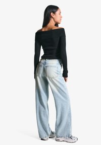 Črna rebrasta majica brez naramnic, kombinirana s svetlo modrimi širokimi kavbojkami. Kavbojke imajo zadnje žepe in bled stili denim. Obuti srebrni superge.