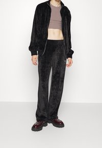 Zwart velours trainingspak met een jas met ritssluiting en broek met elastische tailleband. Gestructureerde stof, voorzien van geribbelde manchetten en een aangesloten cropped top.