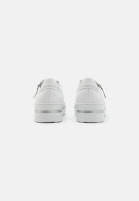 White sneakers featuring a smooth leather upper, subtle silver accents, and a thick sole with a transparent strip at the midsole.