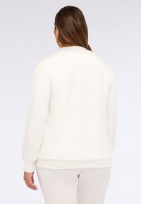 Světle krémová mikina s jemnou texturou, dlouhými rukávy a žebrovanými manžetami. Má zaoblený výstřih a decentní boční pruhy.