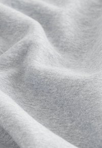 Lichtgrijze stof met een zachte, gladde textuur, waarop een uniforme breipatroon en een zachte val te zien zijn. Ideaal voor casual kleding of textiel.