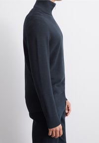 Marinblå zip-up tröja med hög krage, ribbad textur och figurnära design. Har långa ärmar och en enfärgad mönster.