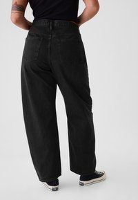 Musta korkeavyötäröinen farkku, jossa leveät lahkeet, kaksi takataskua ja hieman teksturoitu kangas. Yhdistetty mustiin tennareihin.