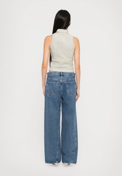 Striped sleeveless top with high collar, paired with wide-leg blue denim jeans featuring back pockets and a loose fit.