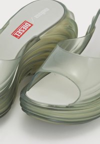 Translucent green slide sandals with a wavy design, open toe, and thick sole. Features logo on insole and smooth, glossy texture.
