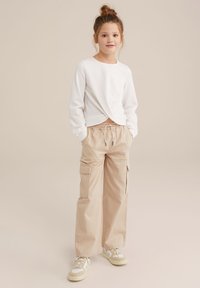 Vit strukturerad långärmad topp med vriden front, kombinerad med beige cargobyxor med sidofickor och elastisk midja. Sneakers med accentfärger.