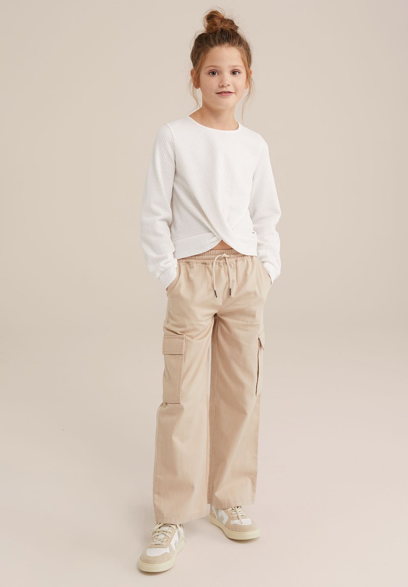 Vit strukturerad långärmad topp med vriden front, kombinerad med beige cargobyxor med sidofickor och elastisk midja. Sneakers med accentfärger.